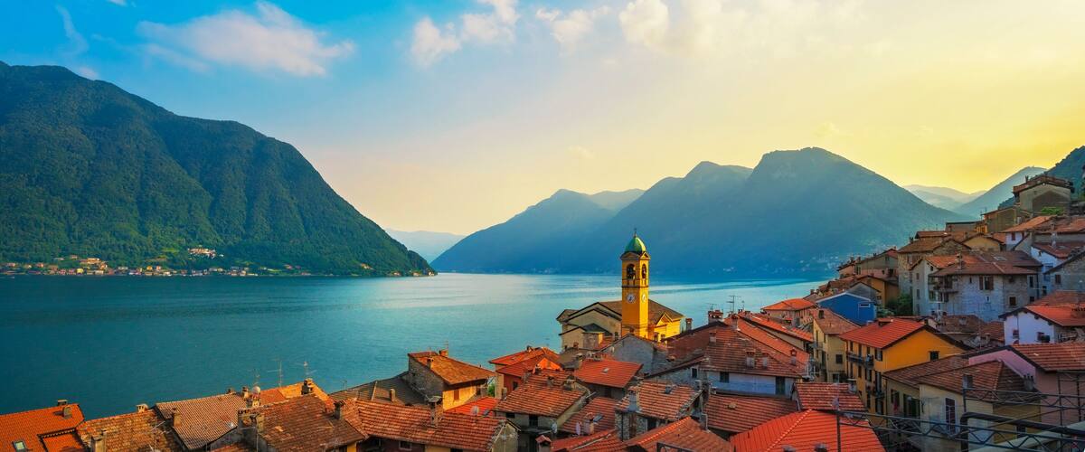 A coastal town with red-roofed buildings, a prominent yellow tower, and mountains in the background.