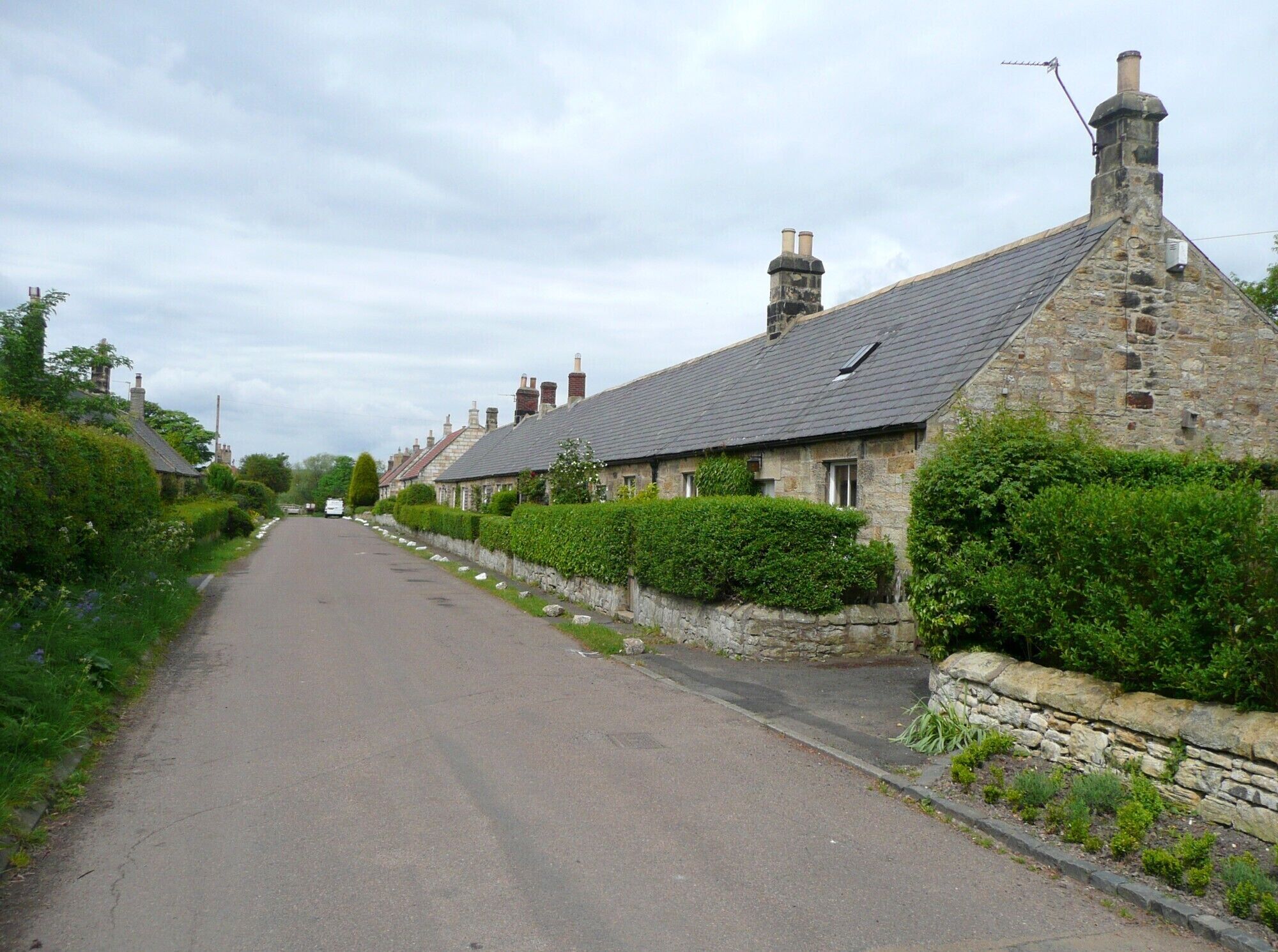 A narrow rural road flanked by stone houses with sloped roofs and chimneys.
