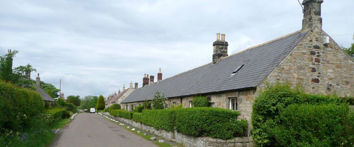 A narrow rural road flanked by stone houses with sloped roofs and chimneys.