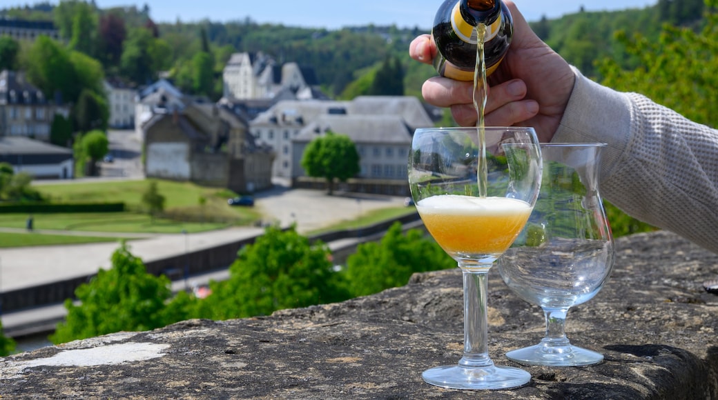 Pouring of blond strong Belgian abbey beer in to glass in sunny day with nice view on old town Bouillon, Belgium