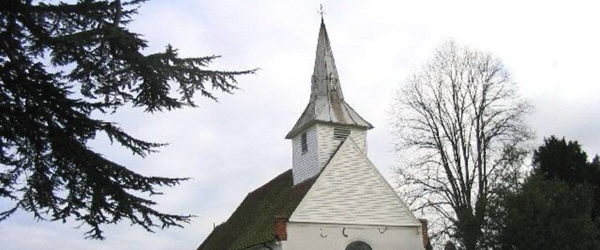 A white church with a pointed steeple and a clock on the front wall, surrounded by a cemetery with headstones.