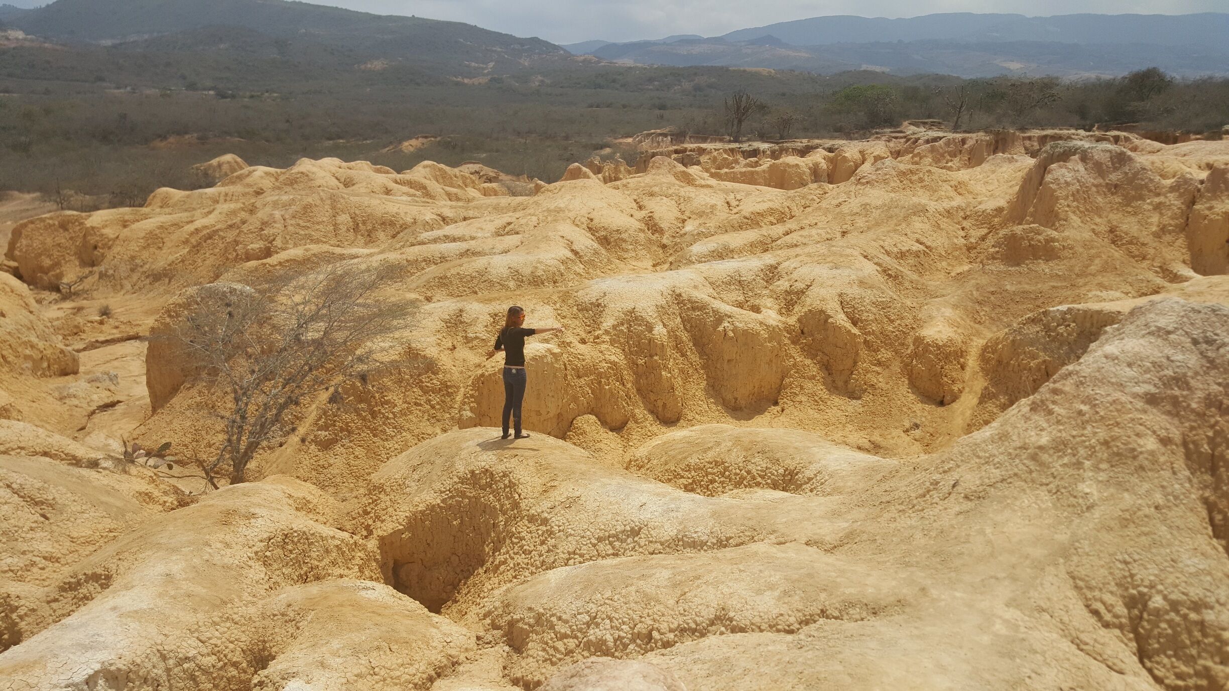 A person standing in a dry, rocky landscape with eroded hills and sparse vegetation.