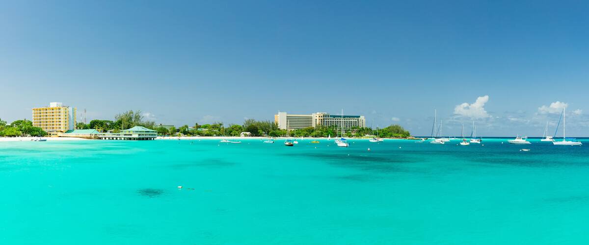 A coastal city with clear turquoise waters, several sailboats, and modern buildings.