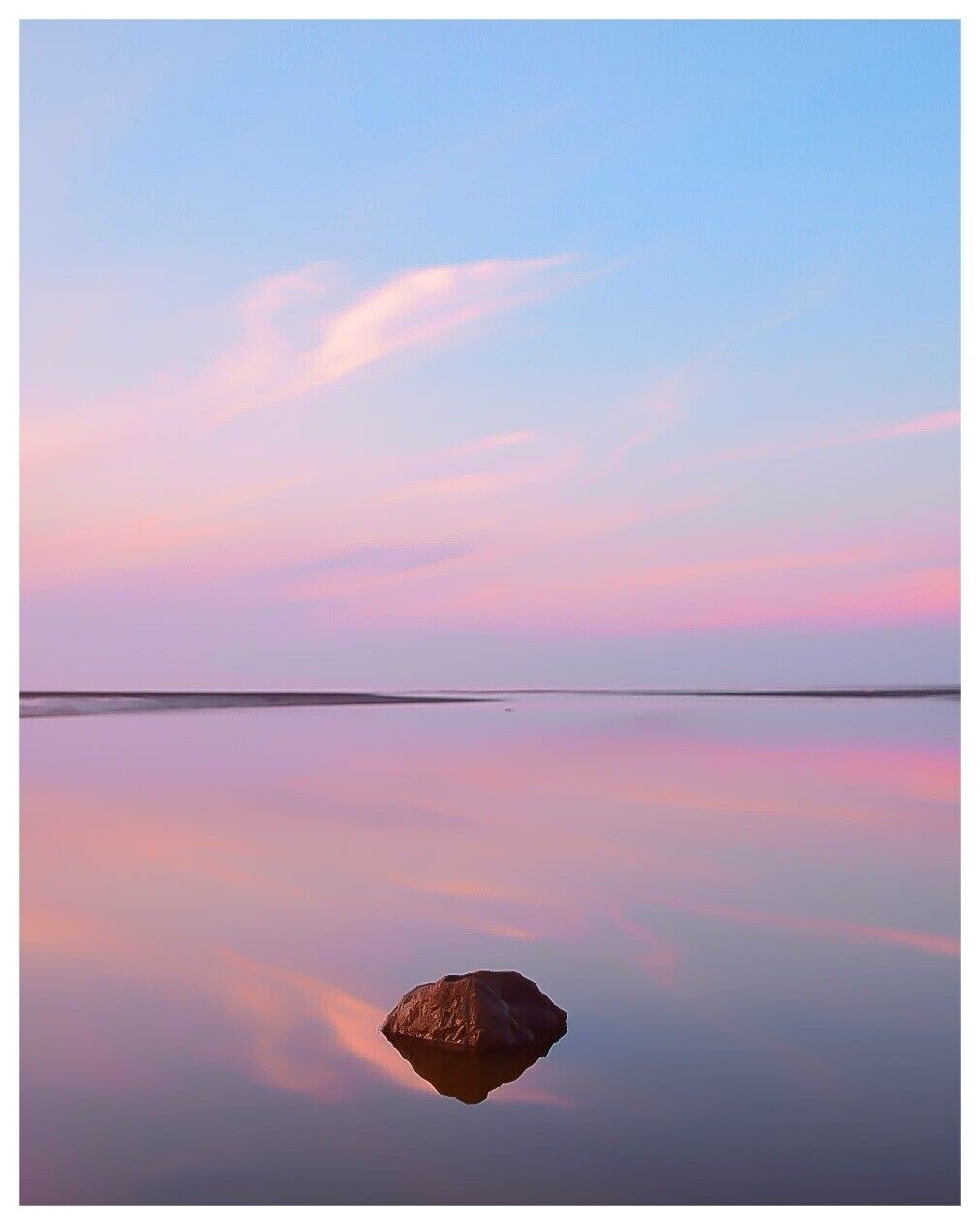 A calm body of water with a single rock in the foreground and a clear sky.