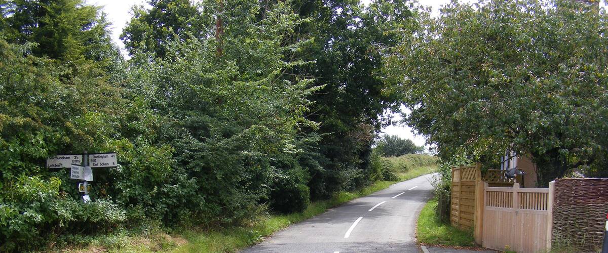 A rural road with directional signs, a wooden gate, and lush greenery.