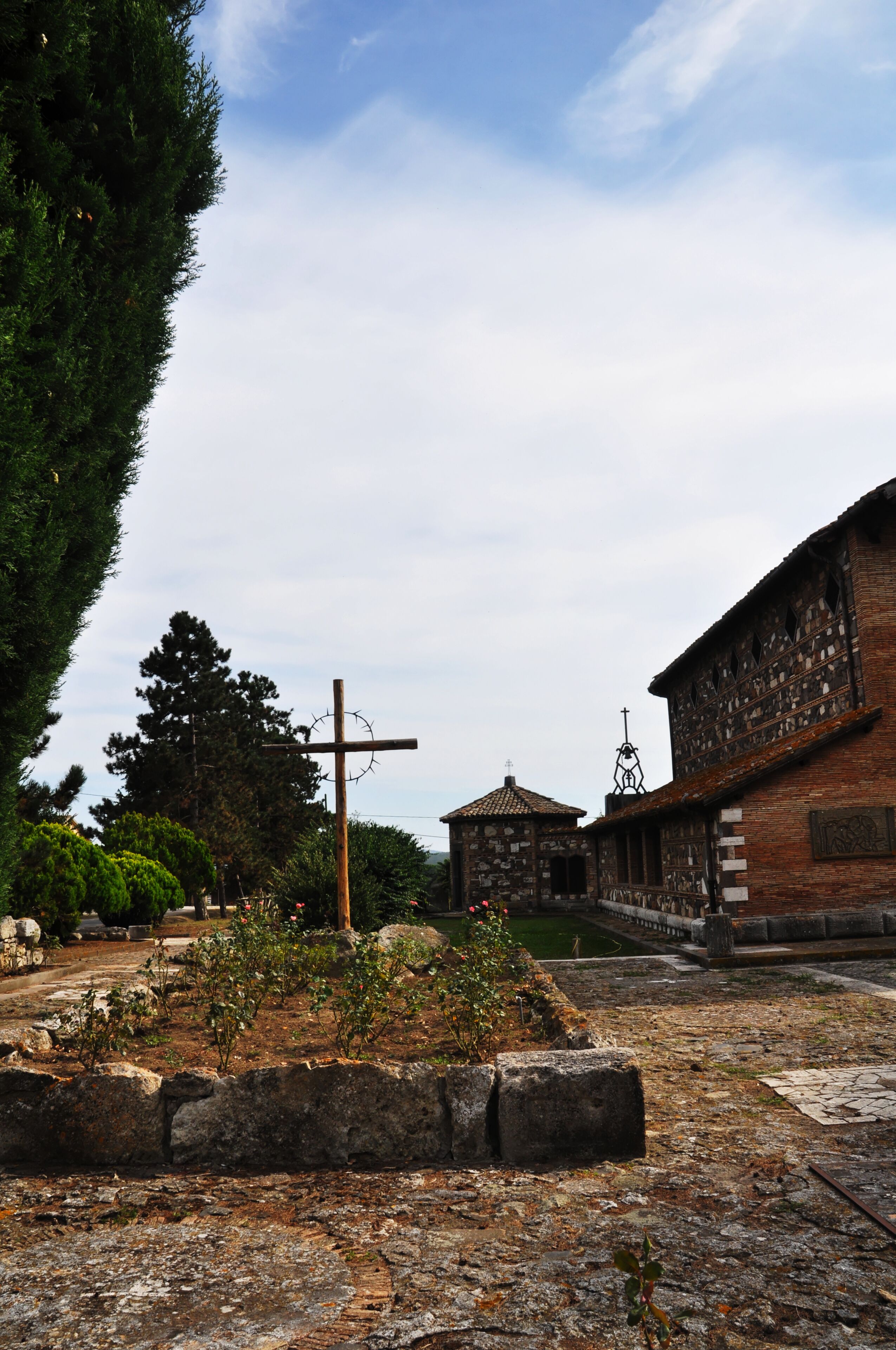 A stone pathway leading to a church with a cross, surrounded by greenery and a clear sky.