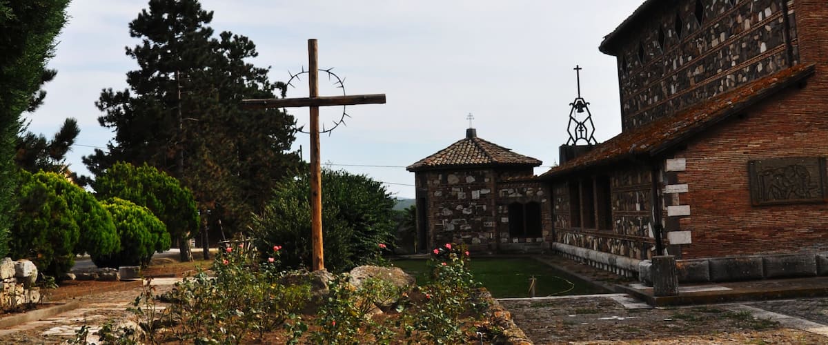 A stone pathway leading to a church with a cross, surrounded by greenery and a clear sky.