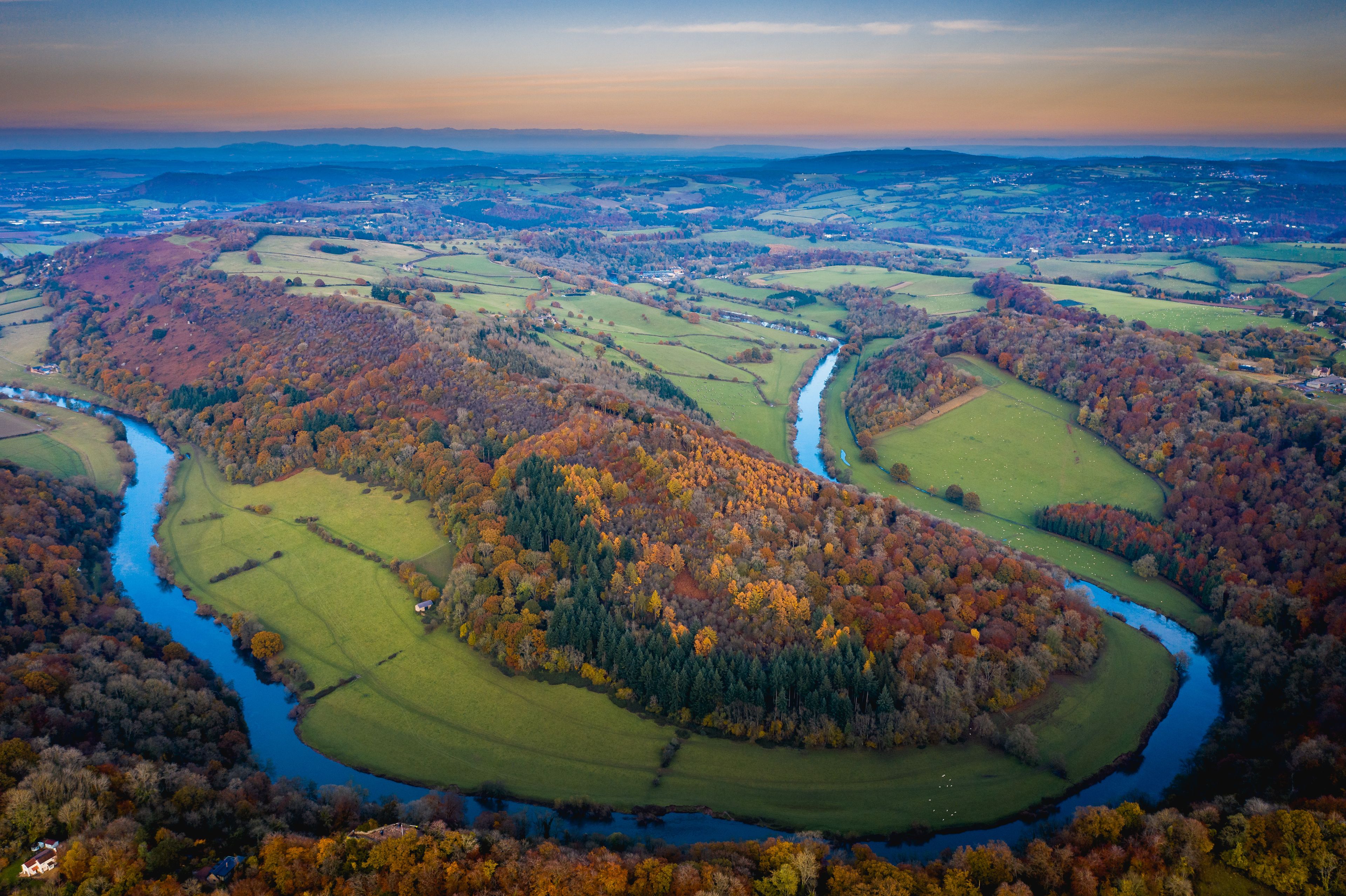 A river winding through rolling hills with autumn-colored trees.