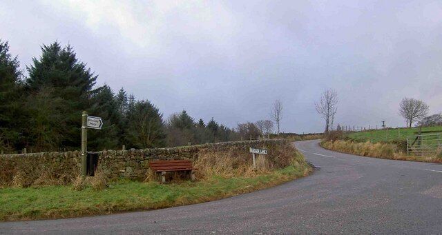 A rural road with a stone wall and a bench.