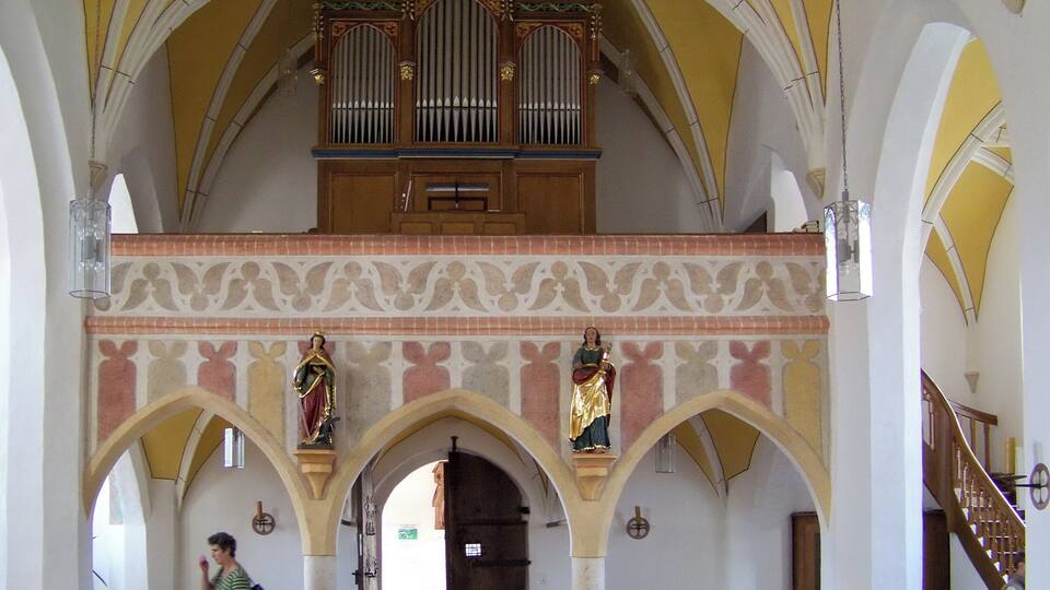 A church interior with a high arched ceiling, a wooden organ, and religious statues.
