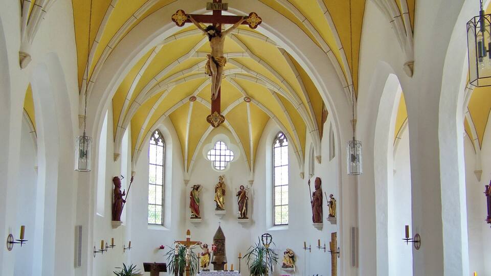 A church interior with a crucifix, arched ceilings, and religious statues.