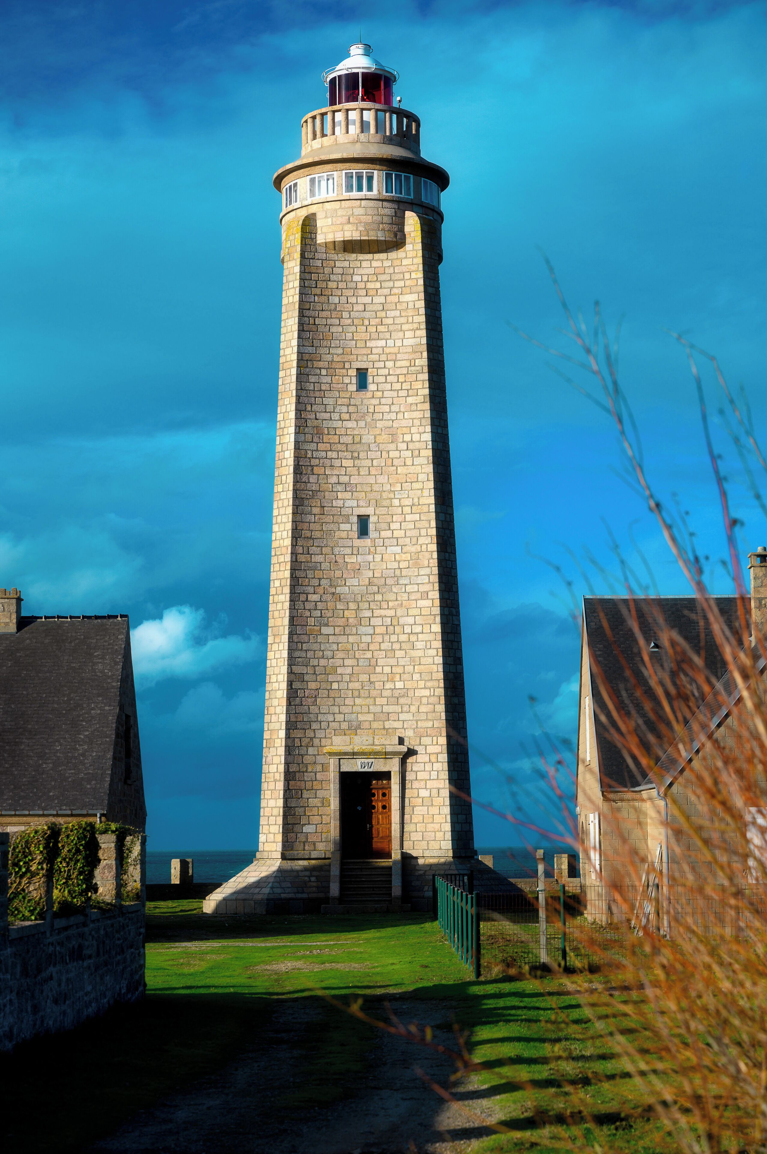 A tall, stone lighthouse with a red and white top, surrounded by a grassy area and a body of water in the background.