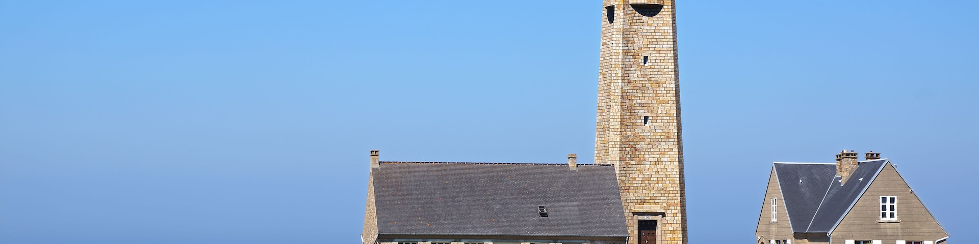Un faro, un edificio de piedra y un campo de flores moradas.