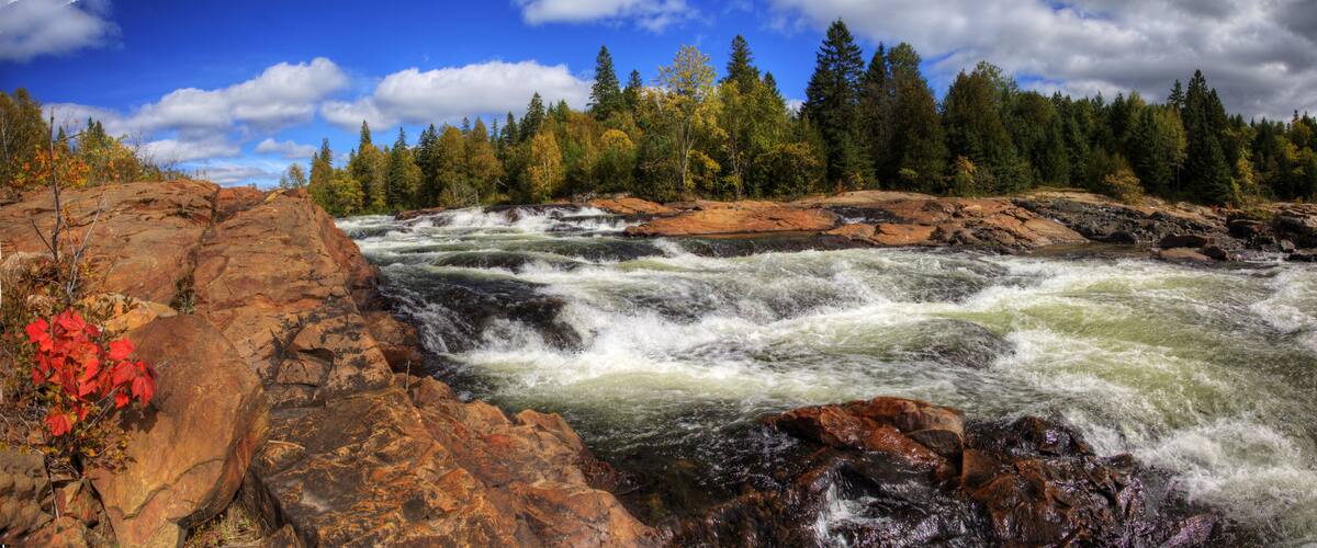A river with white water rapids surrounded by rocky terrain and autumn-colored trees.