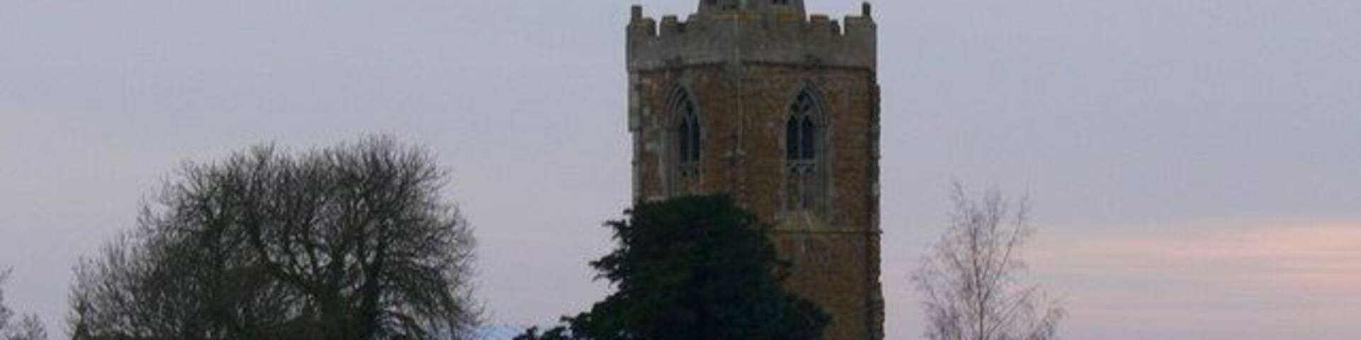 A church with a tall tower and a barn in a rural setting.