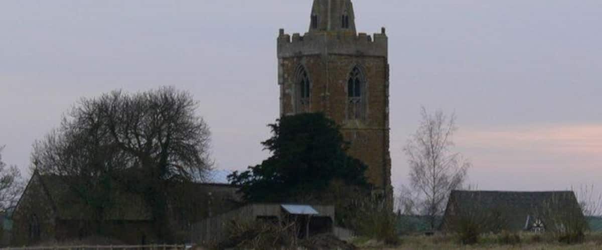 A church with a tall tower and a barn in a rural setting.