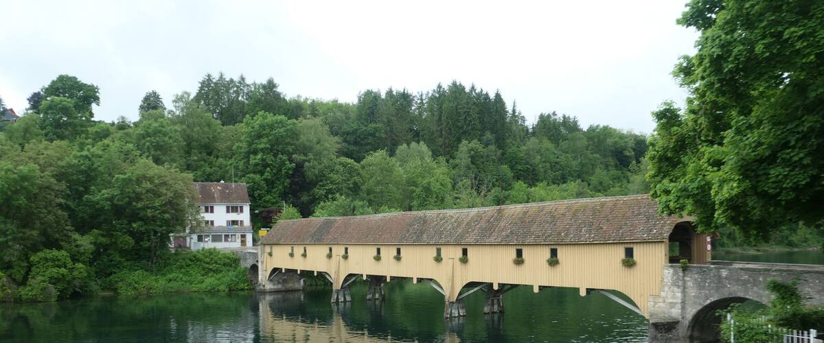 A covered bridge over a river with a house in the background.