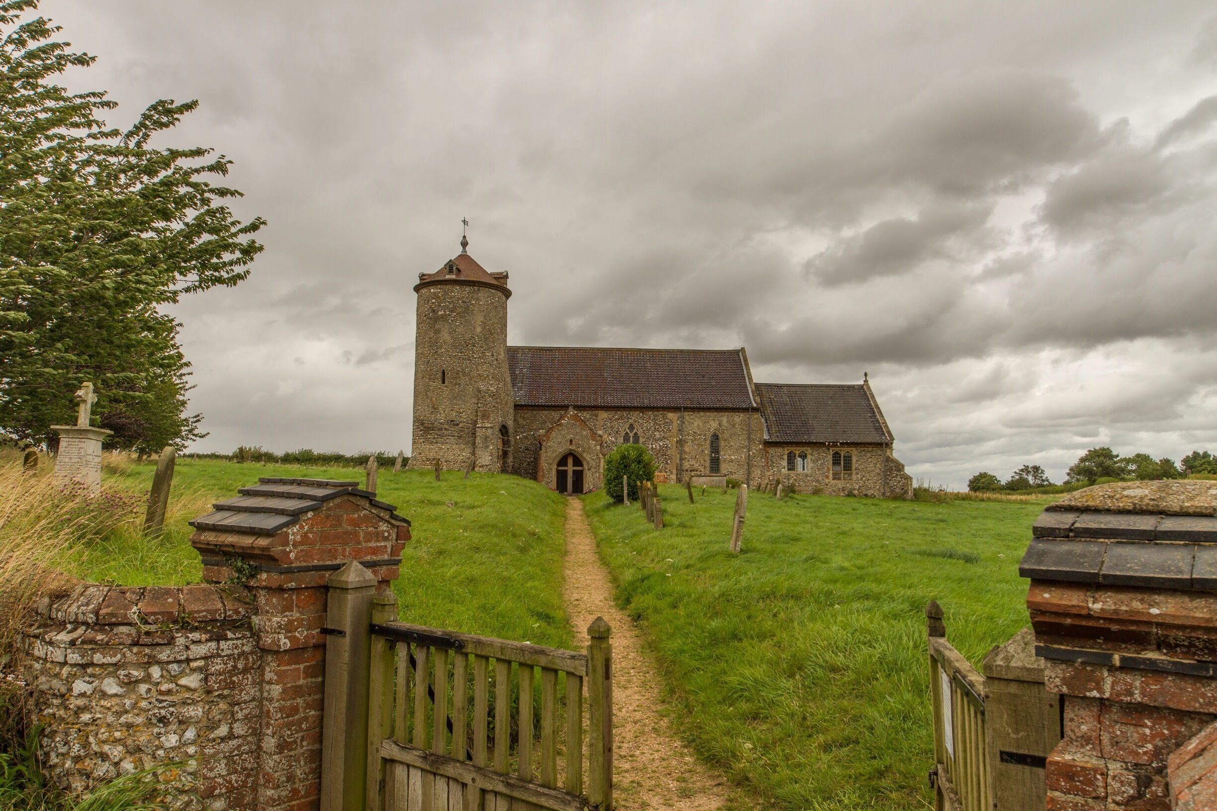 A historic stone church with a tower, surrounded by a grassy field and a stone wall.