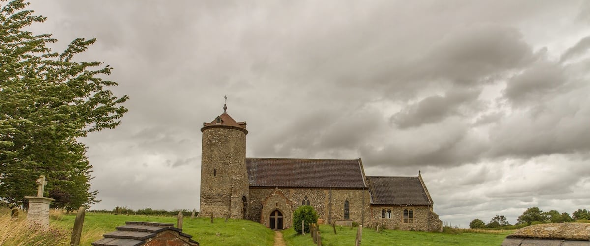 A historic stone church with a tower, surrounded by a grassy field and a stone wall.