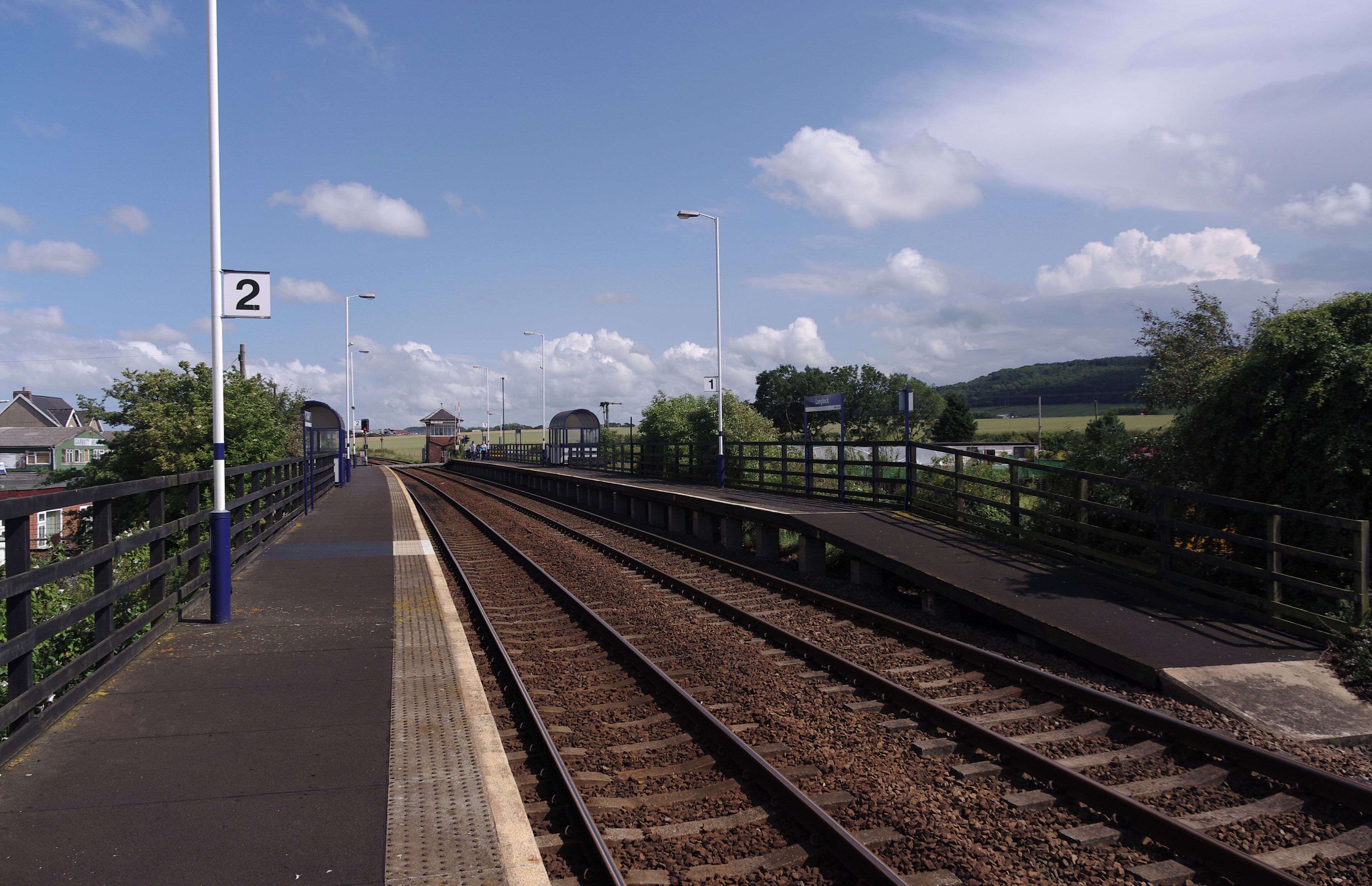 A railway platform with tracks, a blue fence, and a clear sky.