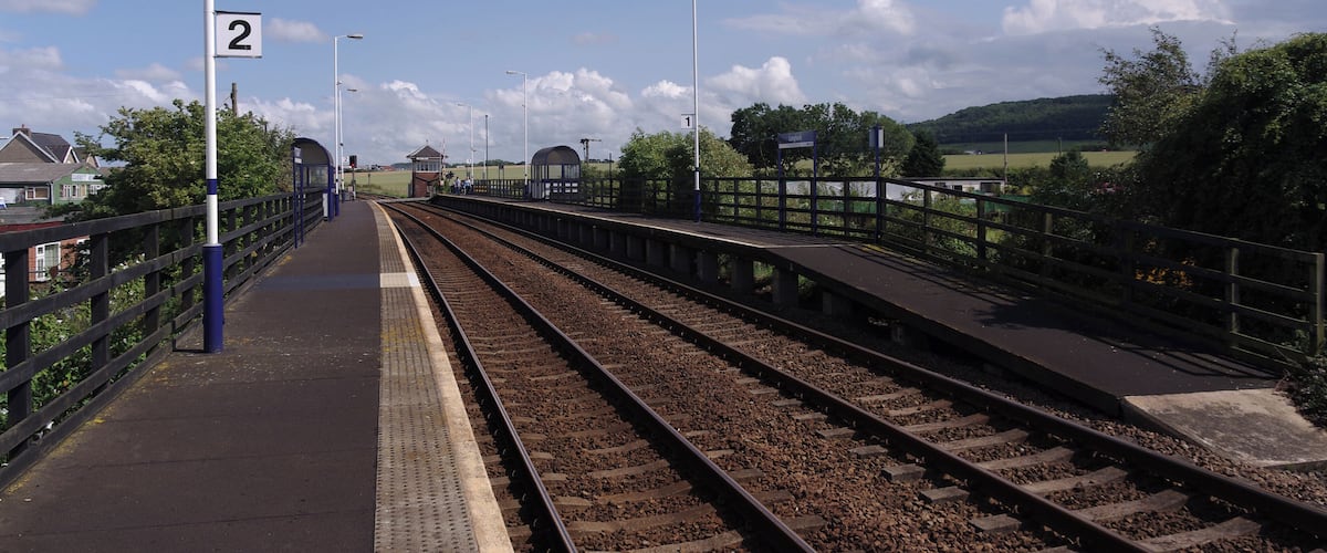 A railway platform with tracks, a blue fence, and a clear sky.