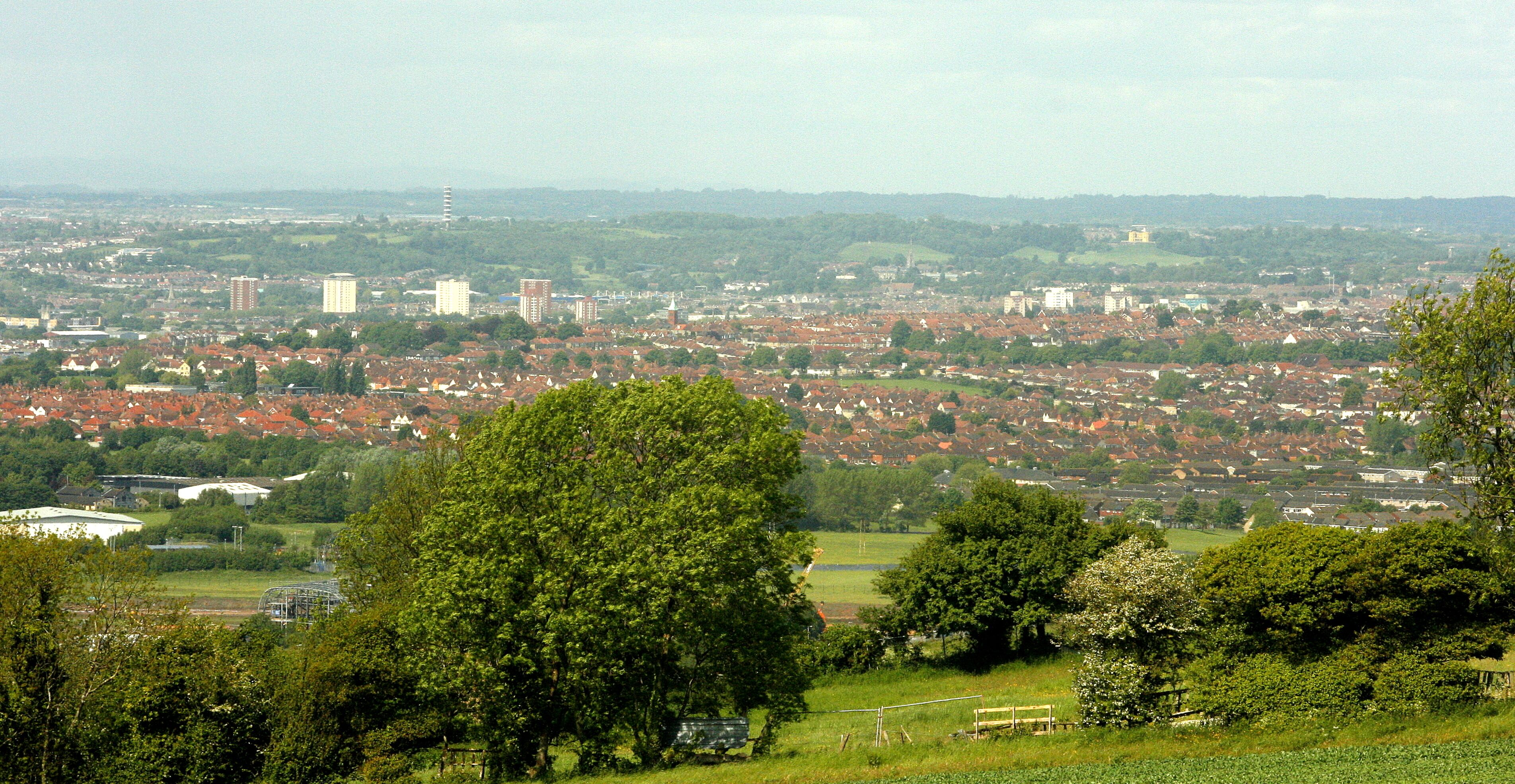 A cityscape with dense residential areas, green hills, and scattered buildings.