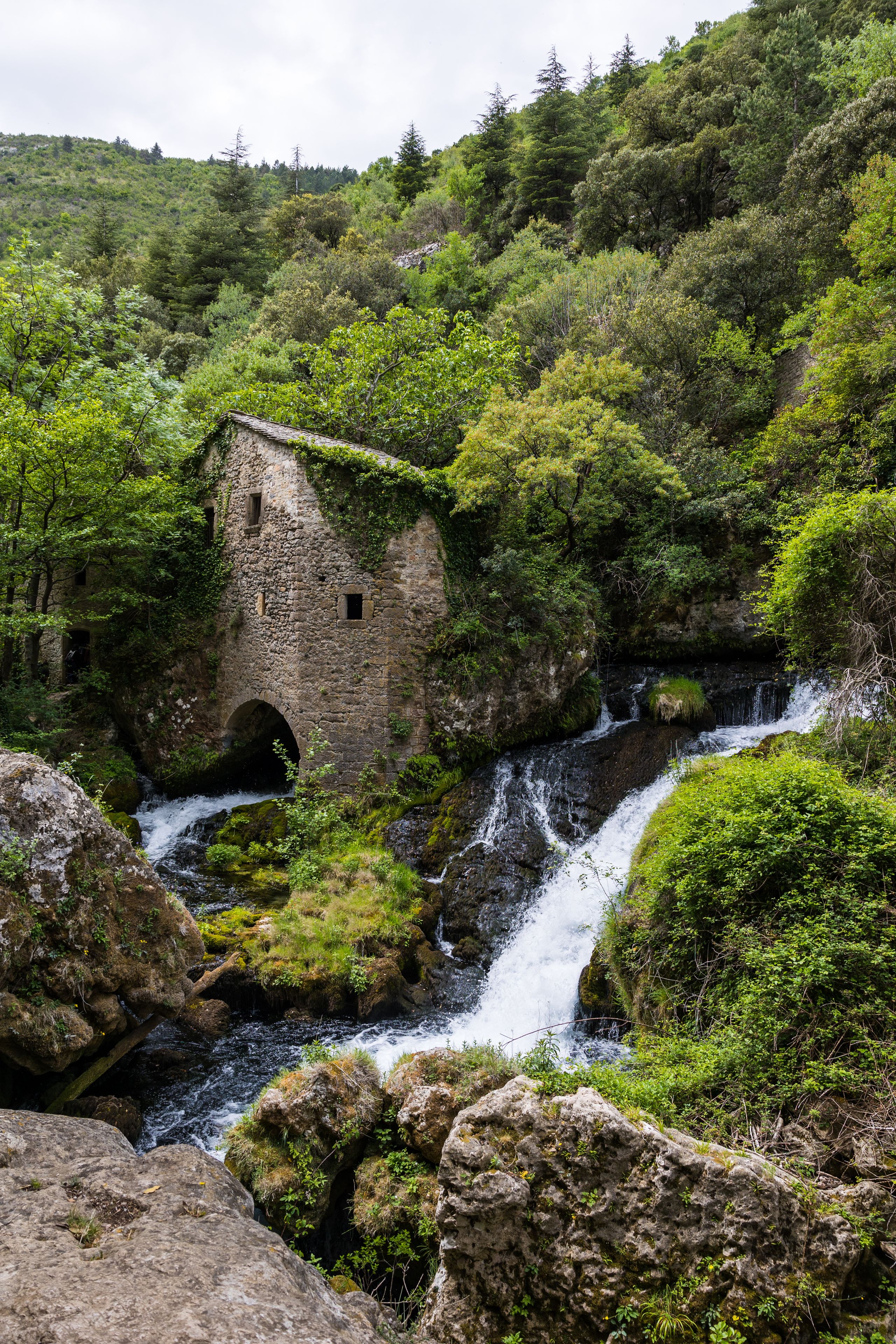 A stone building surrounded by lush greenery and a cascading waterfall.