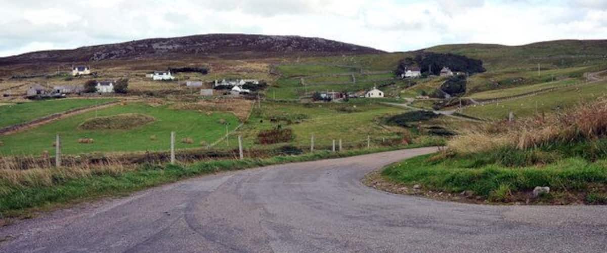 A rural road winding through a hilly landscape with scattered houses and fields.