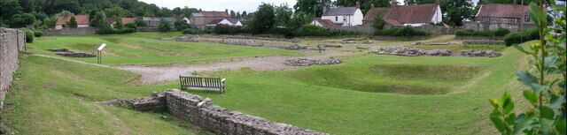 A grassy archaeological site with stone walls and a bench.