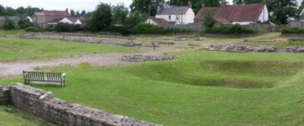 A grassy archaeological site with stone walls and a bench.