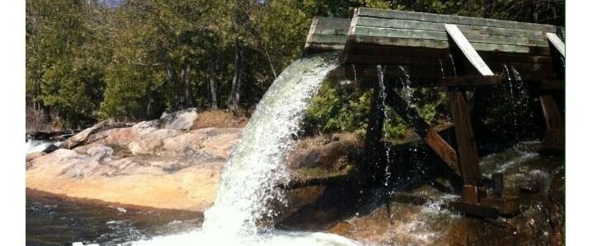 A wooden water spillway over rocks in a forested area.