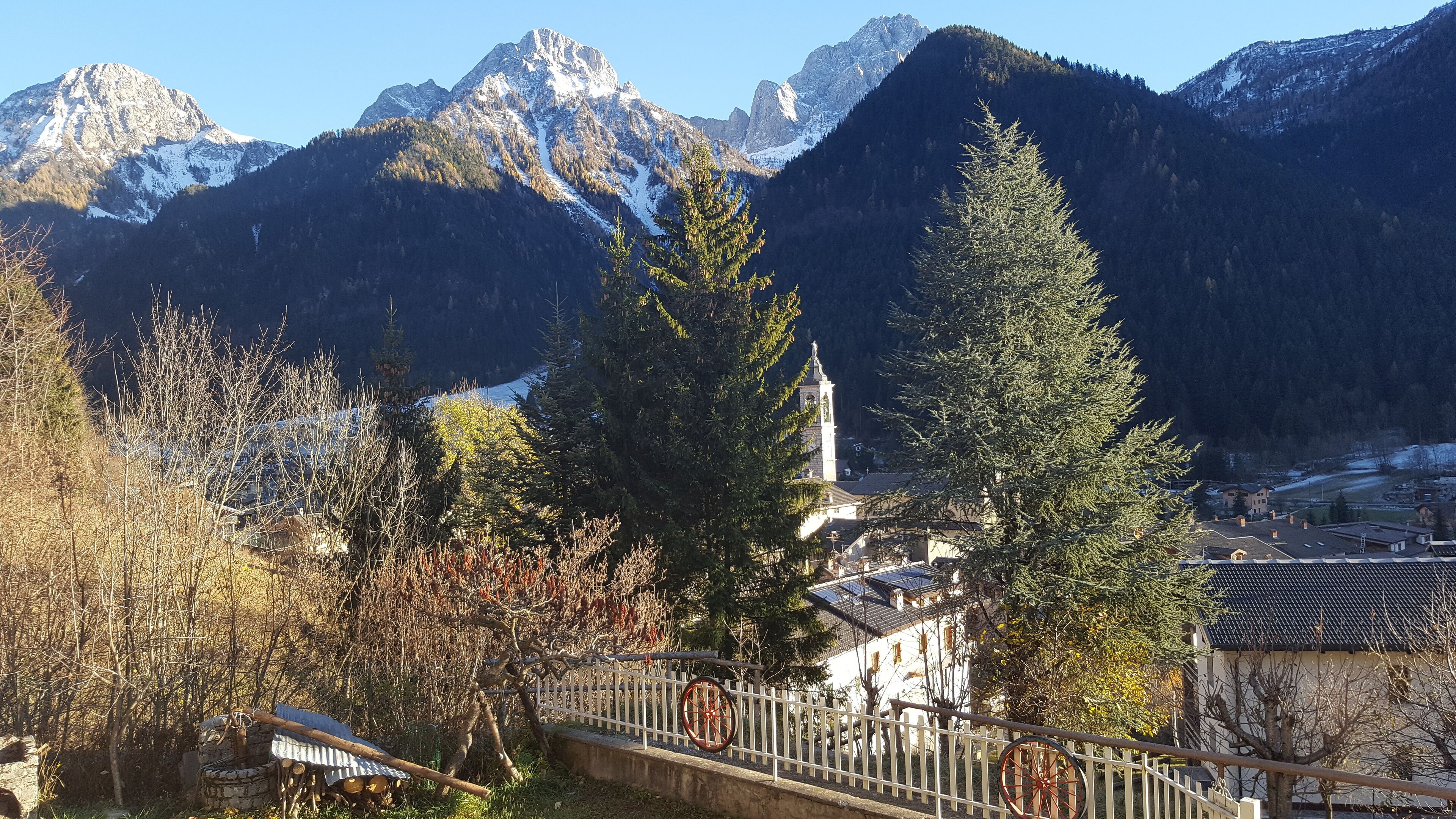A mountainous landscape with a church, trees, and a wooden bridge.