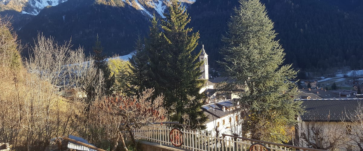A mountainous landscape with a church, trees, and a wooden bridge.
