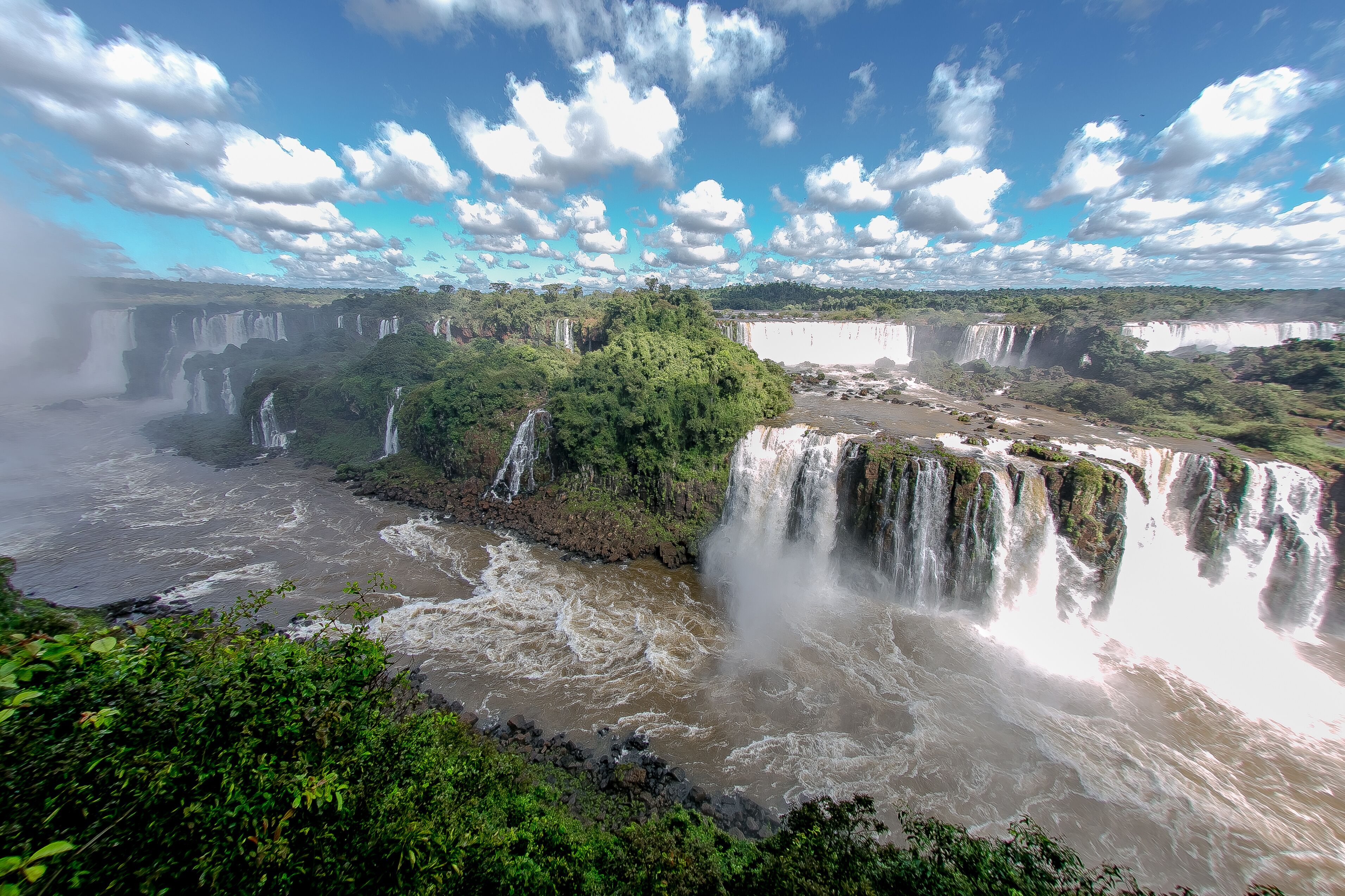 A large waterfall cascading into a river surrounded by lush greenery.