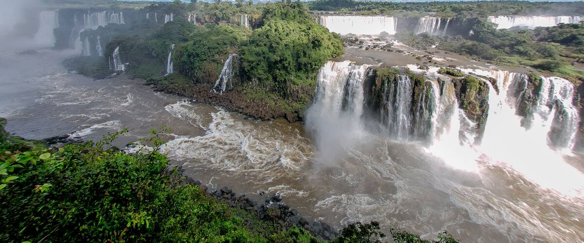 A large waterfall cascading into a river surrounded by lush greenery.