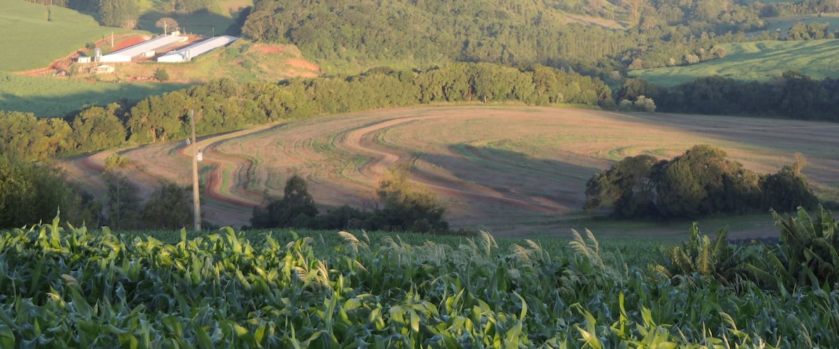 A rural landscape with rolling hills, fields, and a small building.