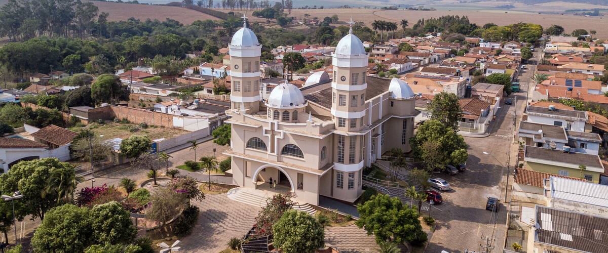 A large church with two domes and a bell tower, surrounded by a town with red-roofed houses and green trees.
