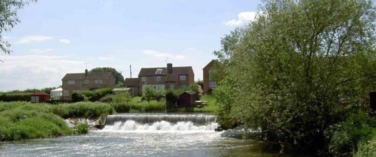 A small waterfall in a residential area with houses and greenery.