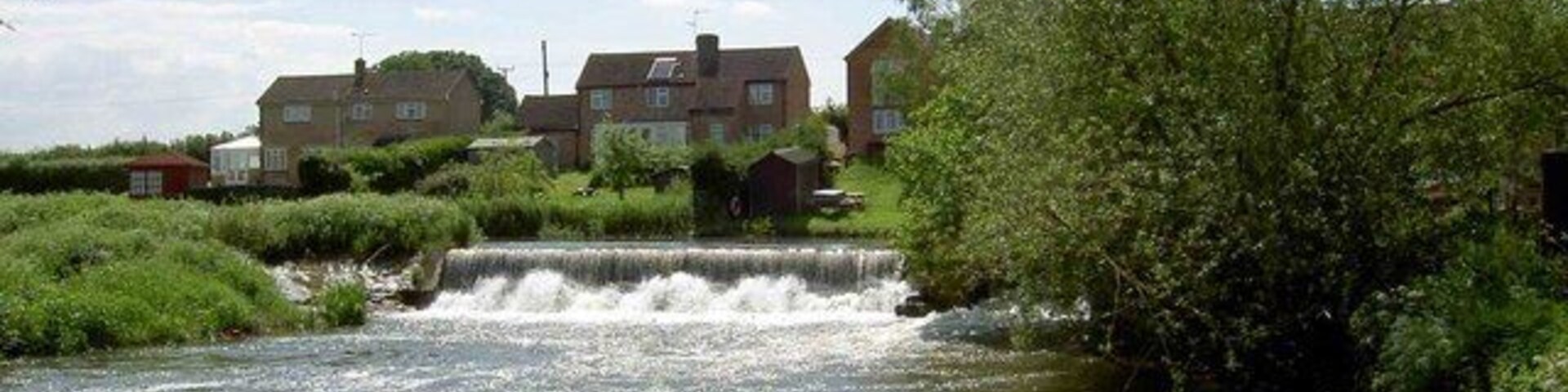 A small waterfall in a residential area with houses and greenery.