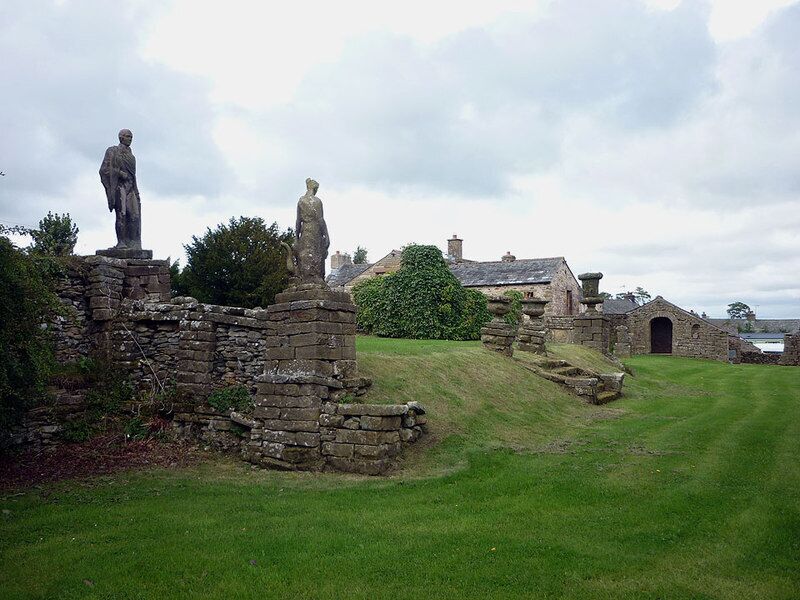 A stone structure with statues, a grassy field, and a building in the background.