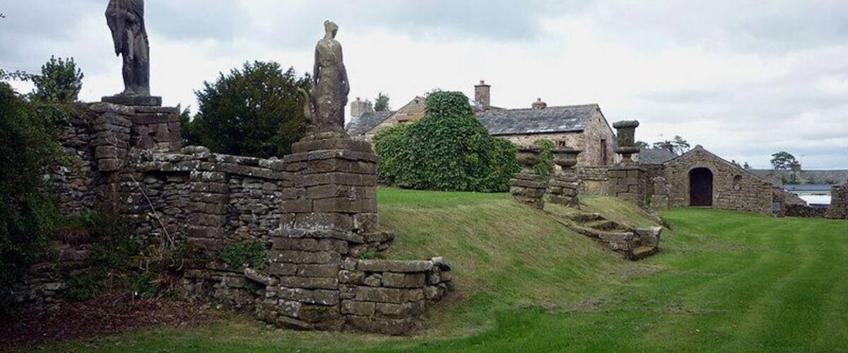 A stone structure with statues, a grassy field, and a building in the background.