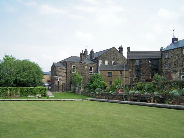 A residential area with stone houses, a well-maintained lawn, and a pathway leading to a gate.