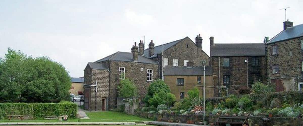 A residential area with stone houses, a well-maintained lawn, and a pathway leading to a gate.