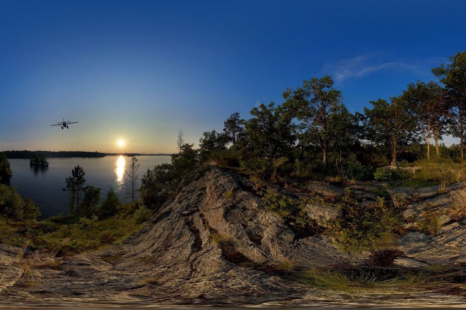 Un atardecer sobre un lago con orilla rocosa y árboles.