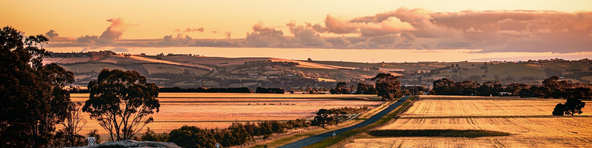 A rural landscape with rolling hills, a winding road, and a sunset.