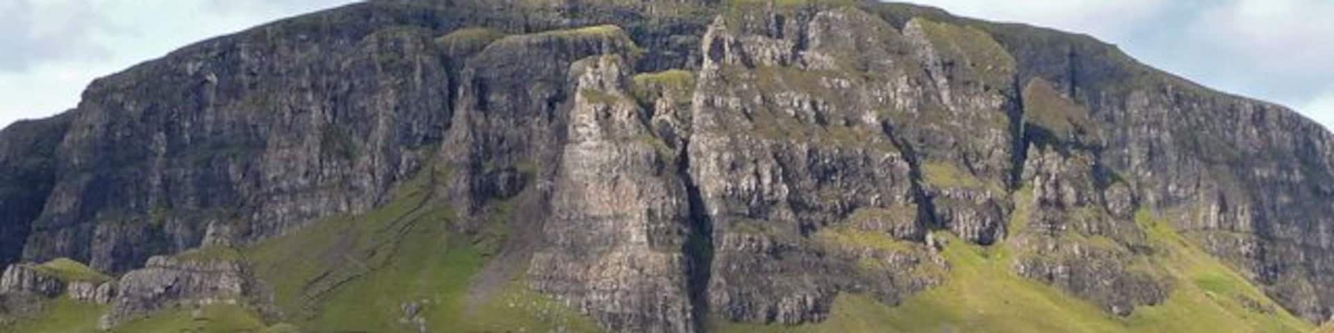 A rugged mountain with steep cliffs and a grassy valley.
