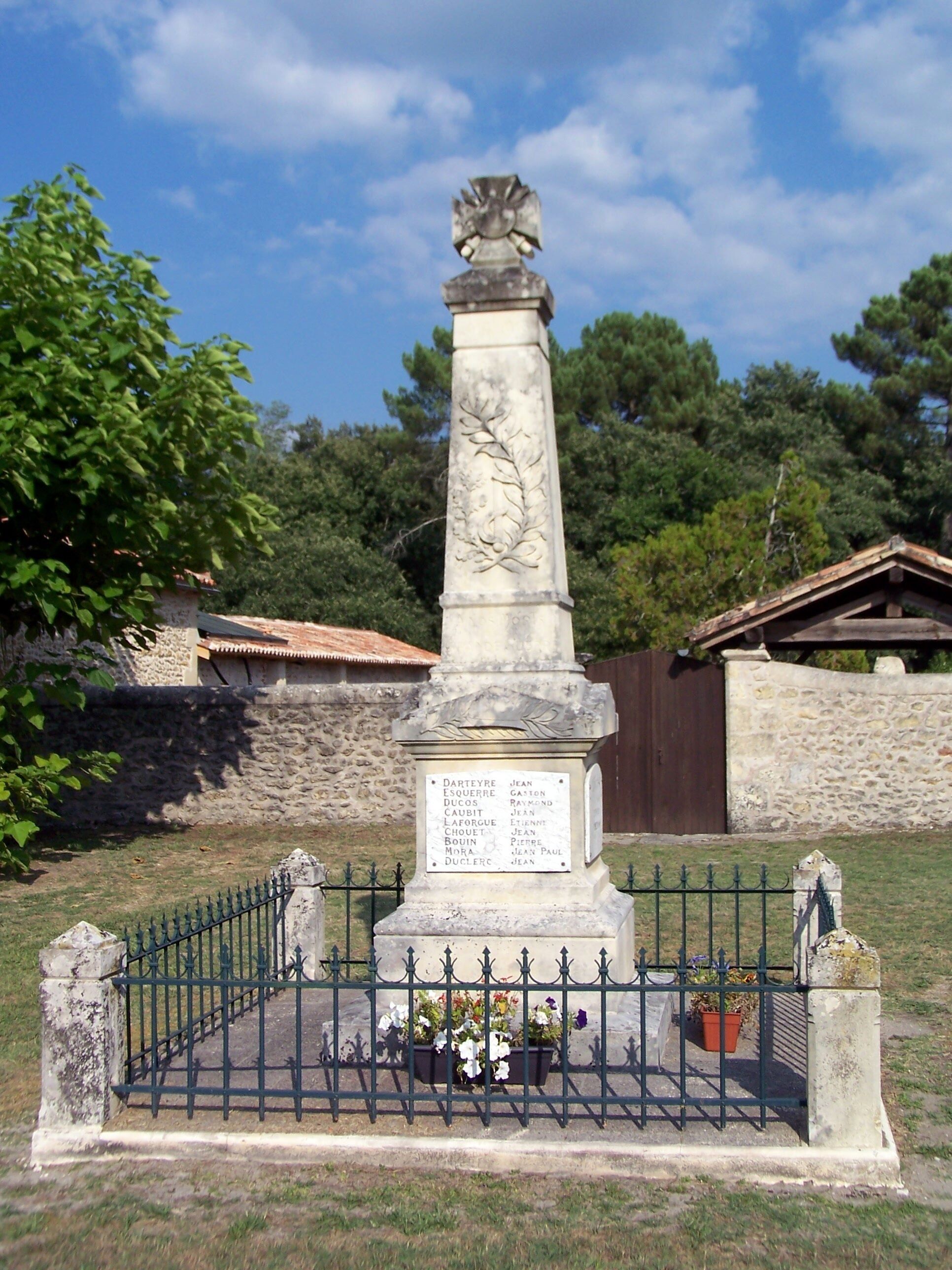 A stone monument with a list of names, surrounded by a metal fence and potted plants.
