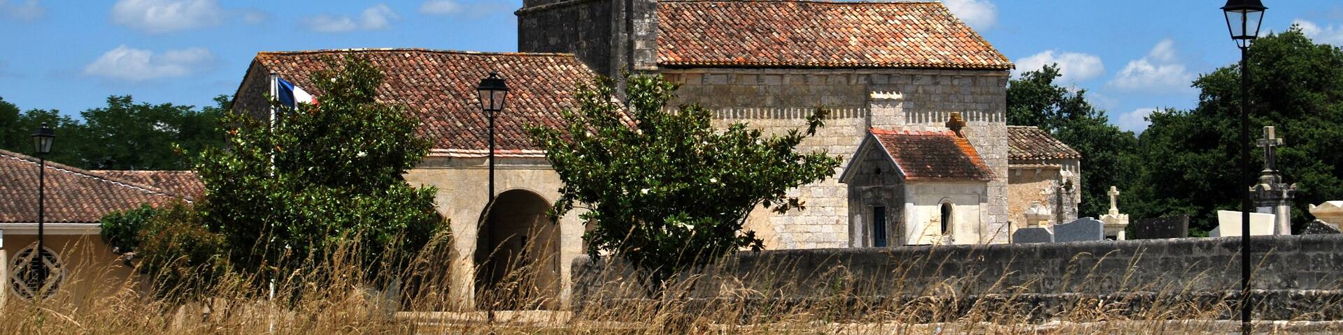 A historic church with a tall bell tower and a tiled roof, surrounded by dry grass and trees.