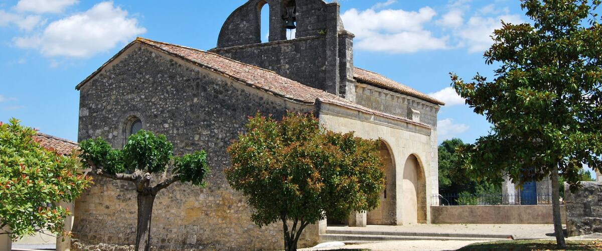 A historic stone church with a bell tower, arched windows, and a cross on top.