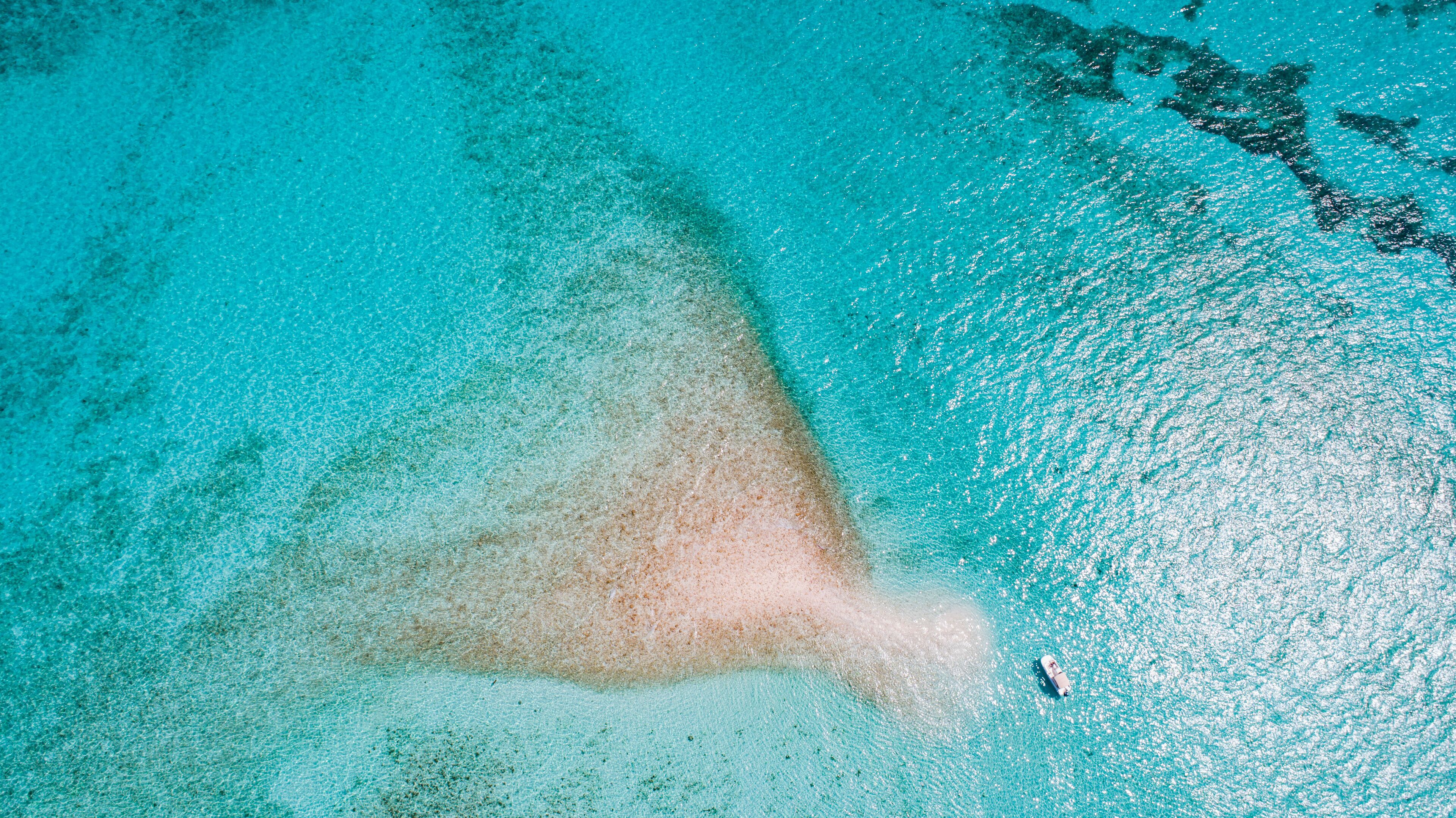 A clear turquoise sea with a sandy beach and a boat.